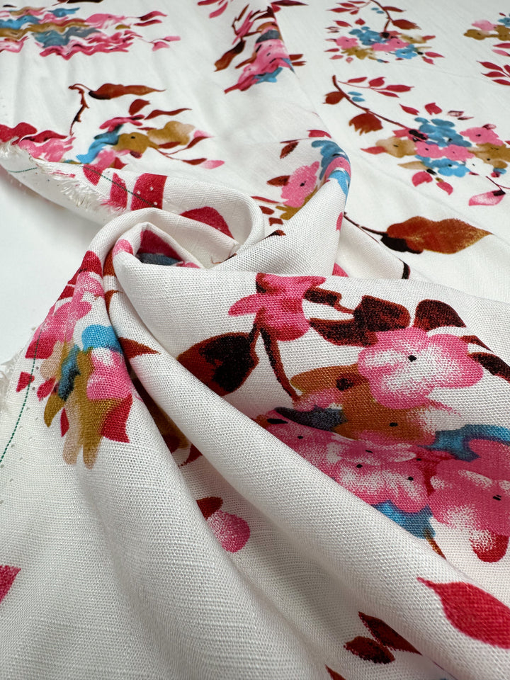 A close-up of Super Cheap Fabrics' Bamboo Rayon - Lil Flower (150cm) shows its lightweight, loosely gathered white fabric with a vibrant pink, red, blue, and brown floral print highlighting the soft texture and drape.