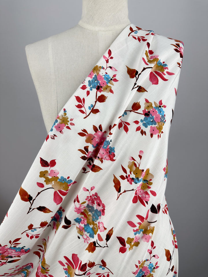 A white mannequin displays Super Cheap Fabrics’ Bamboo Rayon - Lil Flower - 150cm, featuring a lightweight fabric with a colorful floral pattern in pink, red, blue, and gold, set against a plain gray background.