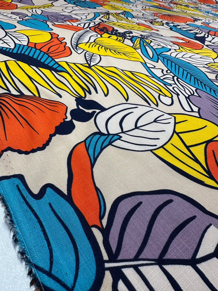 A close-up of Super Cheap Fabrics' Bamboo Rayon - Big Boldy (150cm), featuring a vibrant tropical leaf and flower print in orange, blue, yellow, purple, and black on beige—ideal as a versatile fabric for creative projects.