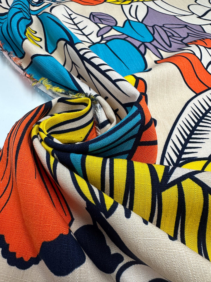 A close-up of Super Cheap Fabrics’ Bamboo Rayon - Big Boldy (150cm), a lightweight fabric in red, yellow, blue, black, and purple floral and leaf patterns on cream, shown slightly wrinkled and twisted at the center.