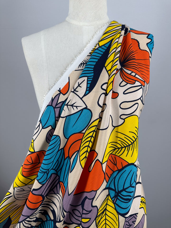 A mannequin displays "Bamboo Rayon - Big Boldy - 150cm" by Super Cheap Fabrics, a soft bamboo rayon with a bold orange, yellow, blue, black, and beige leaf pattern on light background and visible frayed white edge.