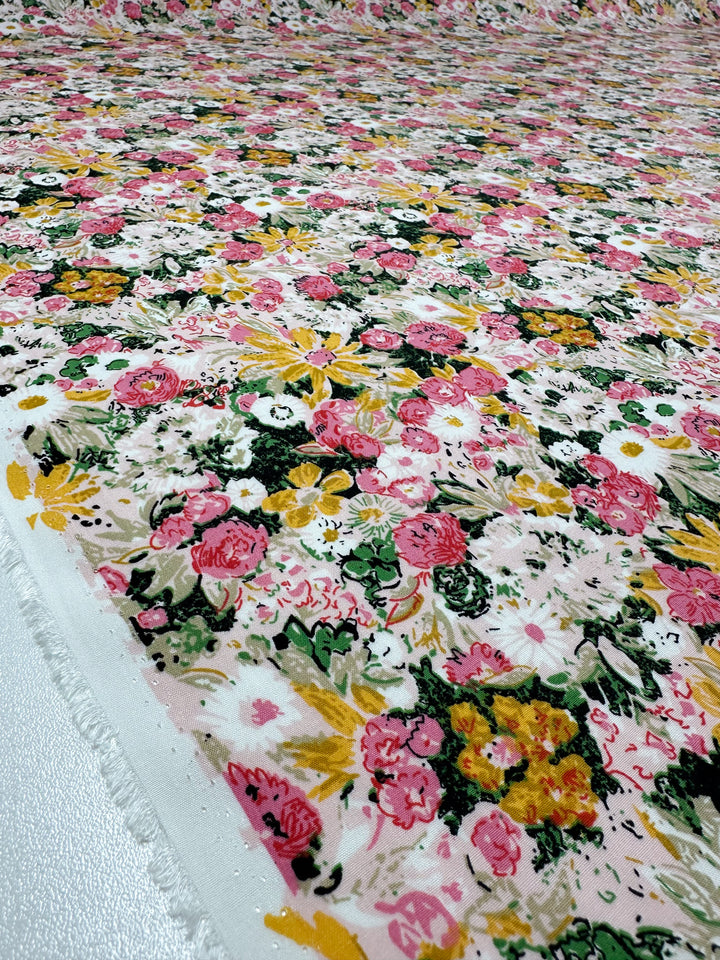 A close-up of Designer Rayon - Floral Garden (145cm) by Super Cheap Fabrics, showing its vibrant pink, yellow, and green floral print on white. The fabric lies flat to highlight its texture and colorful design.