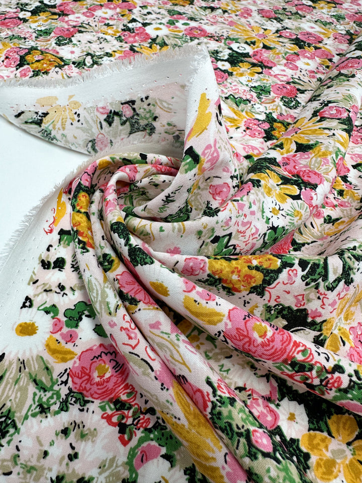 A close-up of Super Cheap Fabrics' Designer Rayon - Floral Garden (145cm), featuring a vibrant pink, yellow, and white floral print with green leaves and soft textured weave—perfect for versatile sewing projects.