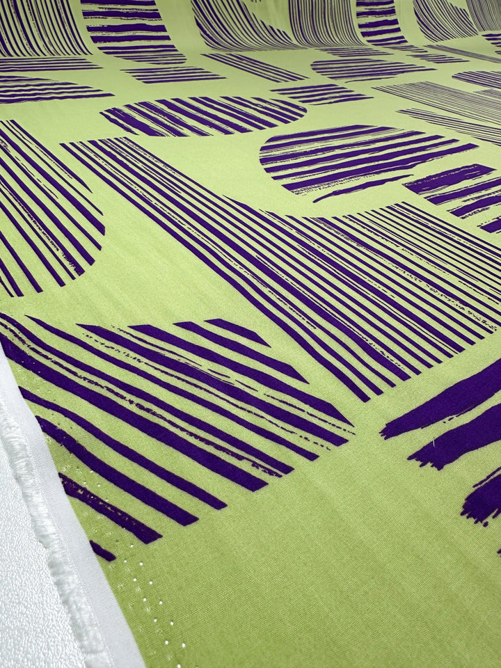 A close-up of Designer Rayon - Geometric Stripes by Super Cheap Fabrics shows bold, irregular dark purple lines and geometric shapes, like circles and rectangles, in a vibrant, modern abstract pattern. Width: 145cm.