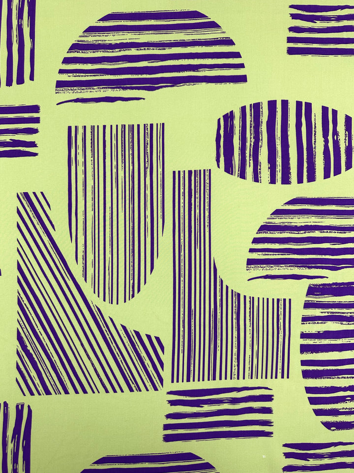 Designer Rayon - Geometric Stripes - 145cm by Super Cheap Fabrics features dark blue circles, rectangles, and diagonal lines with stripes on a light yellow-green background—ideal for vibrant, soft rayon prints.