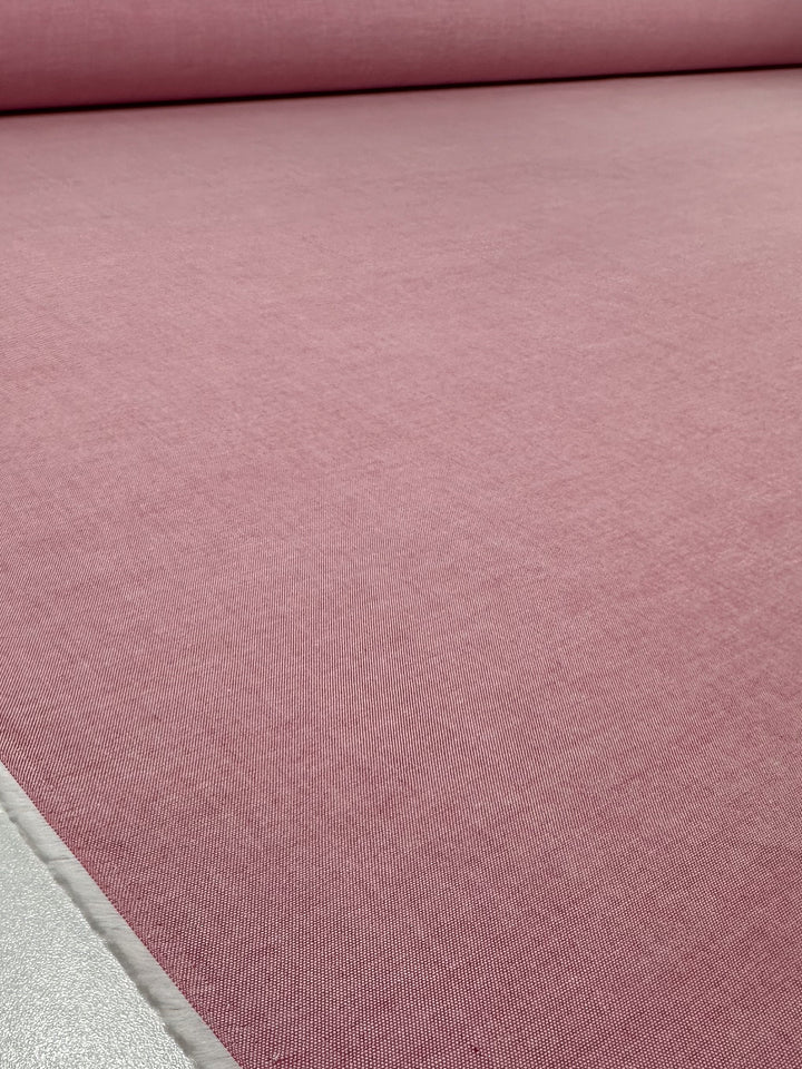 A large roll of Oxford Cotton - Confetti - 146cm by Super Cheap Fabrics in light pink is unrolled on a flat surface, displaying its smooth and even texture with the roll partially visible in the background.