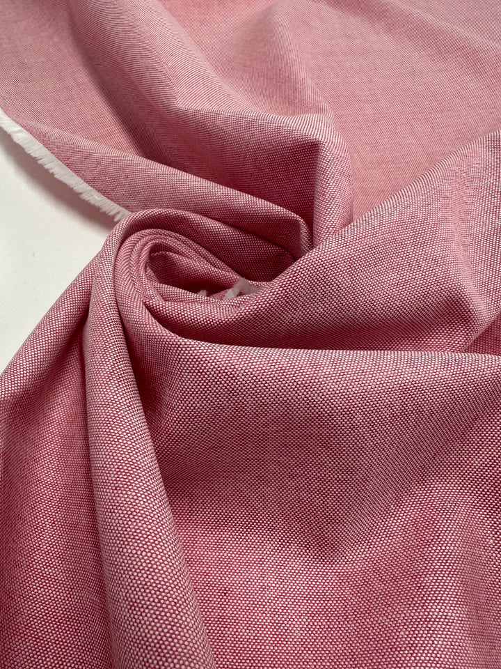 A close-up of Super Cheap Fabrics' Oxford Cotton - Confetti (146cm), a pink, light to medium weight fabric, loosely gathered and folded with visible texture and a slightly frayed edge on the left.
