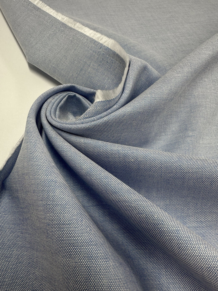 Close-up of Super Cheap Fabrics' Oxford Cotton - Little Boy Blue (146cm), showing soft drapes, subtle woven texture, and a crisp white selvage edge.