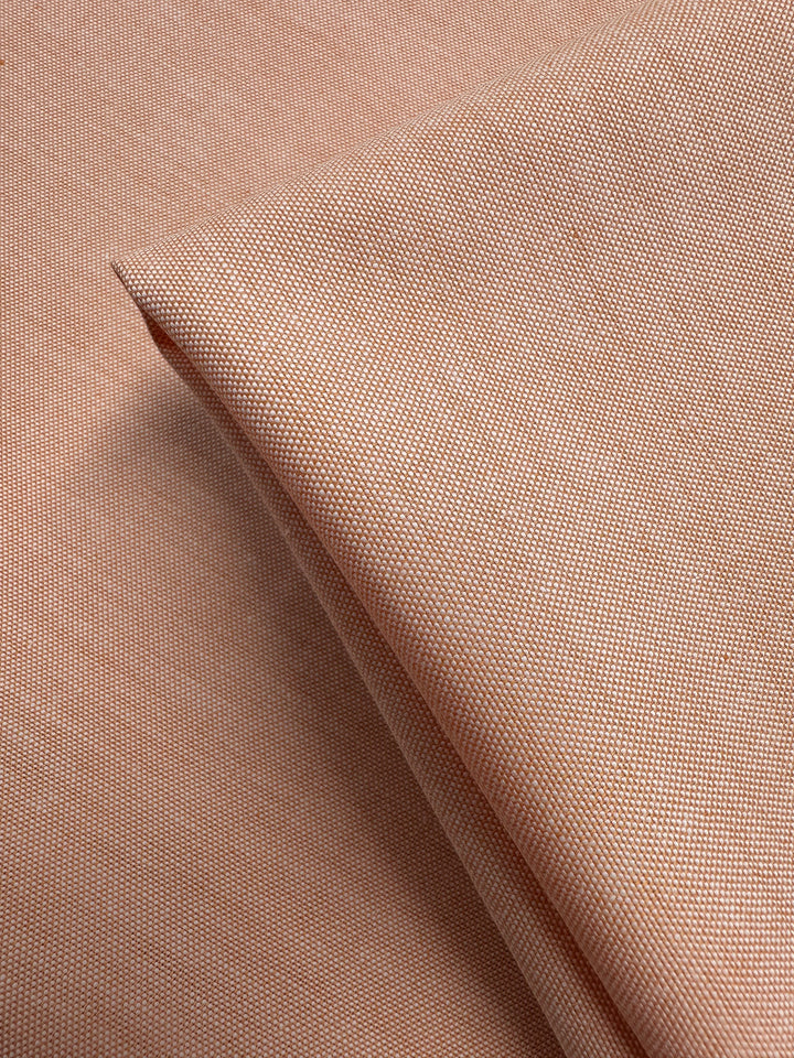 A close-up of Super Cheap Fabrics' Oxford Cotton - Sunburst (146cm) shows its light brown, finely textured weave. The light to medium weight fabric appears smooth with a subtle sheen and is shown folded on a flat surface.