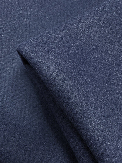 A close-up of Pressed Fleece Coating - Chevron by Super Cheap Fabrics shows folded navy fabric with a subtle chevron pattern and soft texture. This medium weight, 160cm wide fabric combines elegance with versatility.