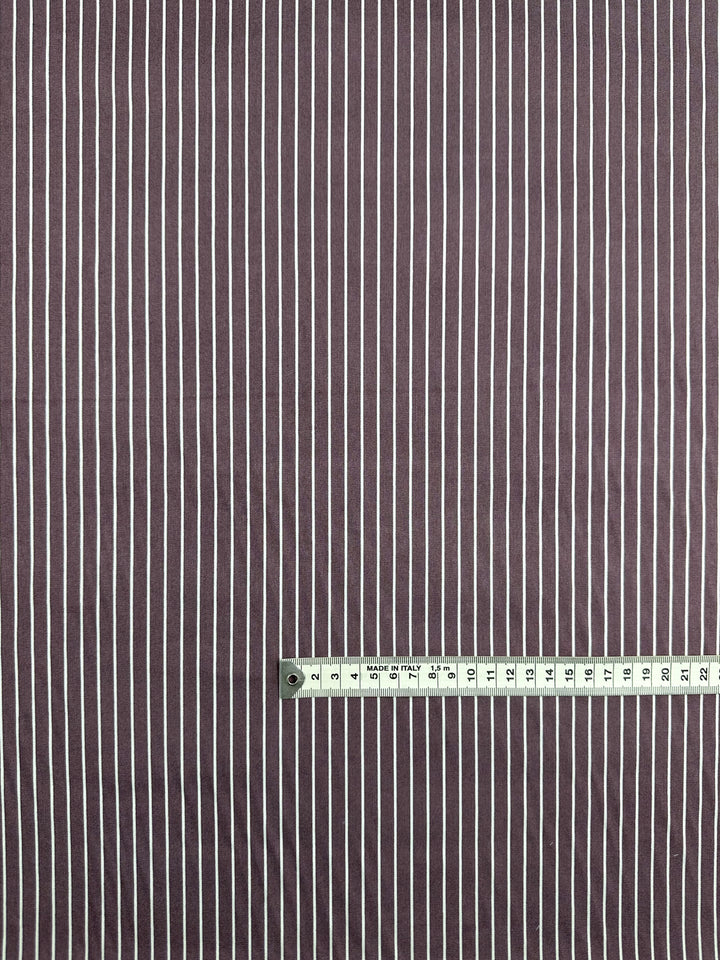 Super Cheap Fabrics' Chambray - Grape Shake - 150cm features maroon fabric with vertical white stripes, shown with a measuring tape along the bottom indicating approximately 23 centimeters in length.