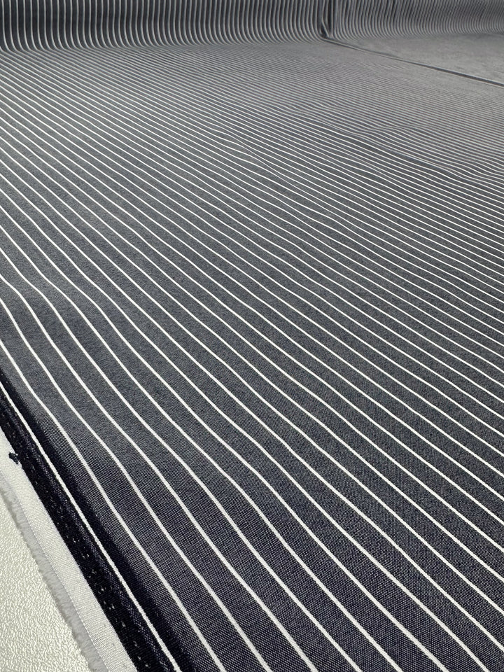 Close-up of Super Cheap Fabrics’ Chambray - Naval Academy - 150cm: lightweight fabric with thin white stripes evenly spaced on a dark gray background, curving slightly at the edges for a subtle striped pattern.