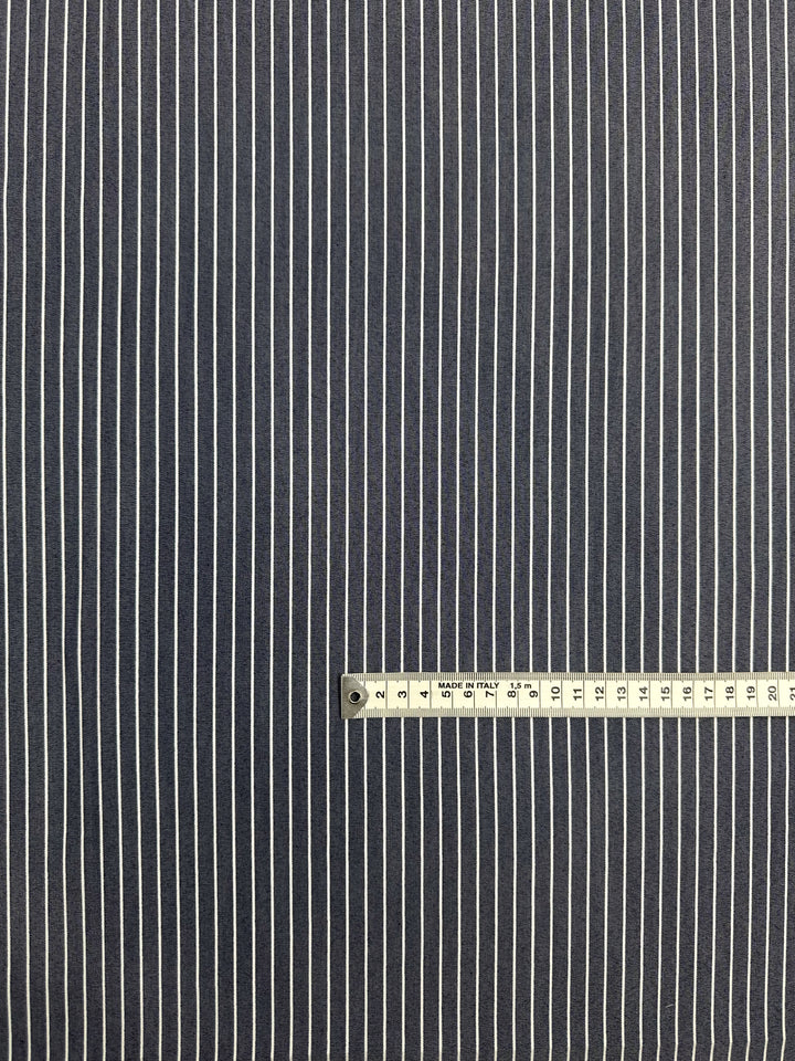 A close-up of Super Cheap Fabrics' Chambray - Naval Academy - 150cm shows blue fabric with evenly spaced vertical white pinstripes. A measuring tape at the bottom indicates a scale of about 15 centimeters.