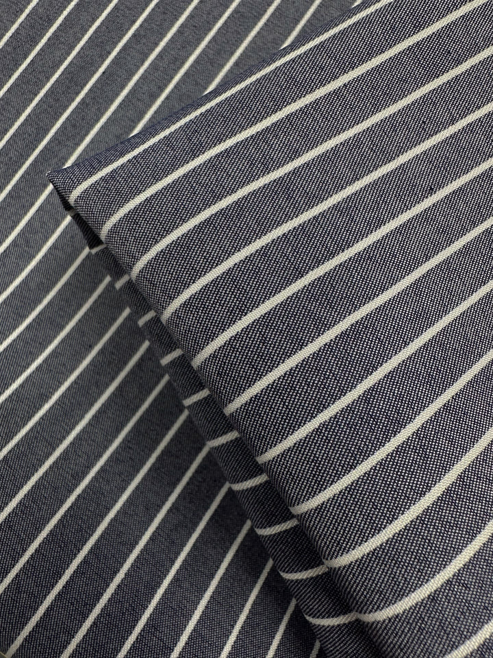 Close-up of Super Cheap Fabrics' Chambray - Naval Academy - 150cm, a lightweight dark blue fabric with thin white stripes. Two layered pieces create intersecting lines and a textured pattern reminiscent of the Naval Academy color.