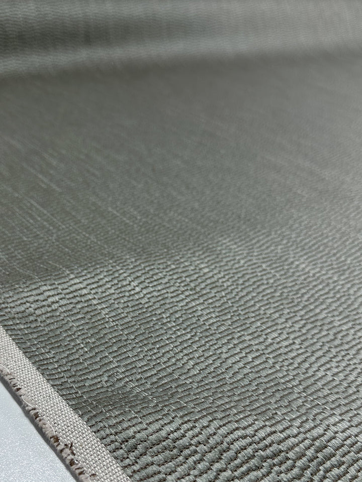 Close-up of Super Cheap Fabrics' Cut Pile Jacquard Upholstery - Oscar Gunmetal (142cm), highlighting its textured gray fabric, visible left-edge seam, fine woven threads, and subtle sheen.