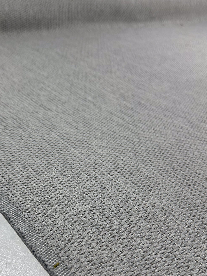 Close-up of Super Cheap Fabrics' Upholstery - Bacchus Silver - 145cm, showing its textured light gray fabric, diagonal seam in the bottom left corner, and a softly blurred background that highlights the high-end quality.
