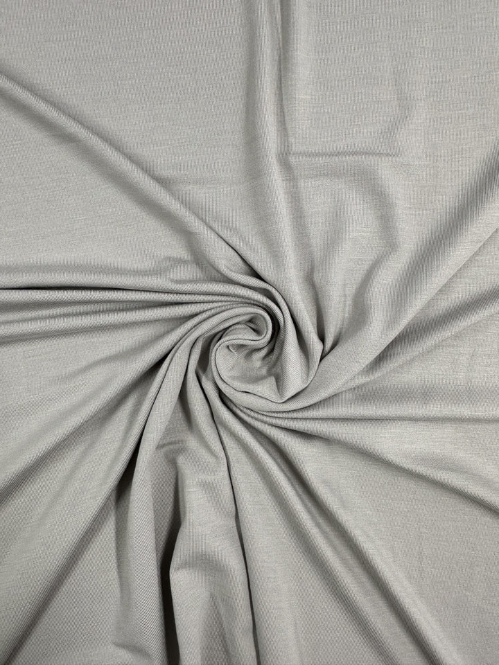 Super Cheap Fabrics’ Cotton Lycra - Moonstruck (168cm) in light gray is spread and gathered at the center, creating a soft spiral of visible folds—ideal stretch fabric for bodycon dresses.