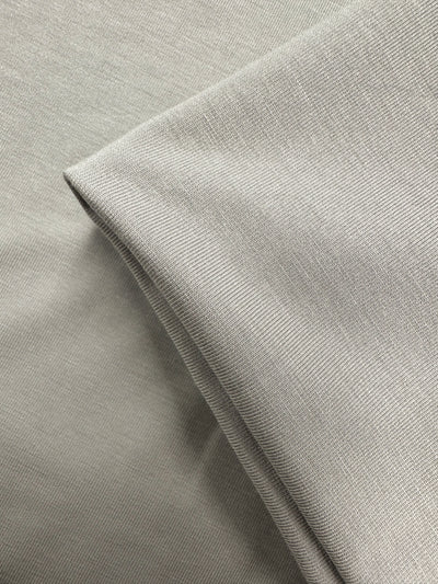 A close-up of Super Cheap Fabrics' Cotton Lycra - Moonstruck (168cm) in light gray, showing its subtle texture with one piece laid flat and another folded neatly on top.