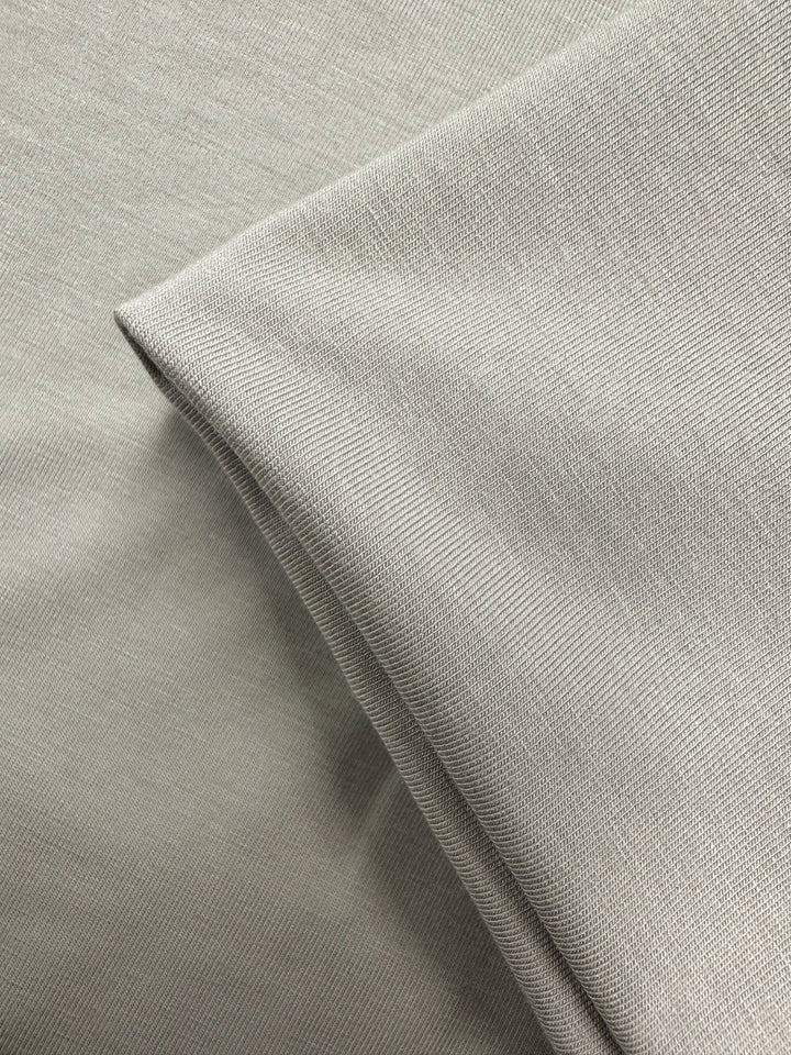 A close-up of Super Cheap Fabrics' Cotton Lycra - Moonstruck (168cm) in light gray, showing its subtle texture with one piece laid flat and another folded neatly on top.