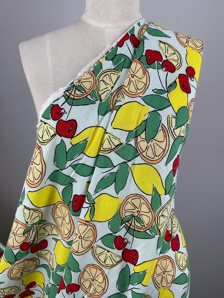 A mannequin displays Super Cheap Fabrics’ Printed Linen Blend - Citrus Crush (134cm), featuring vibrant lemons, cherries, and green leaves on a light background—ideal for summer jackets or lively upholstery projects.