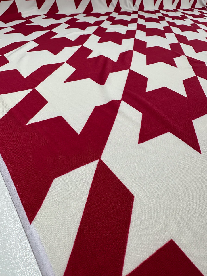 Printed Lycra - Bold Bite - 154cm by Super Cheap Fabrics features a red and white geometric star pattern, offering a bold, angular look on durable, medium-weight fabric.