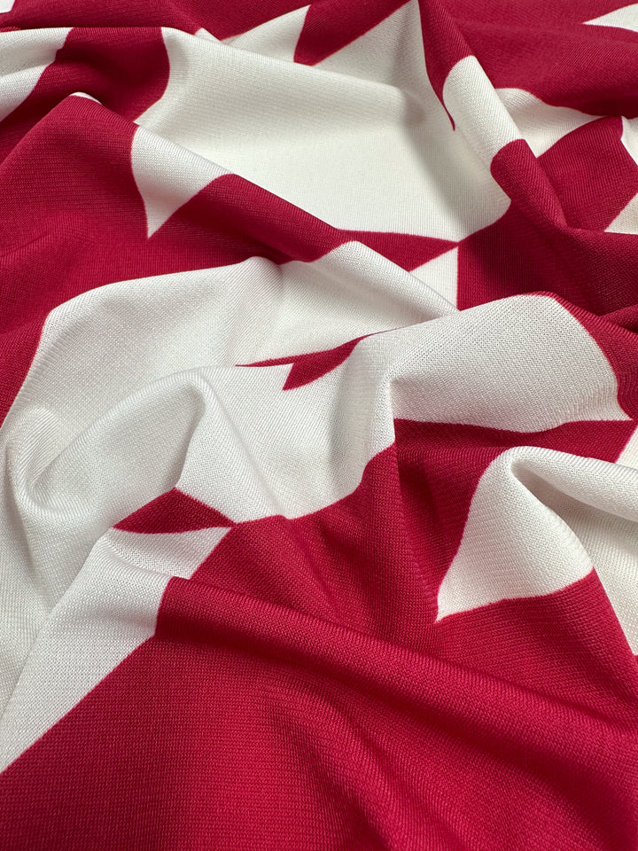 The Super Cheap Fabrics Printed Lycra - Bold Bite (154cm) is a soft, medium-weight fabric with a striking red and white geometric pattern, shown here gently gathered to highlight its texture and drape.