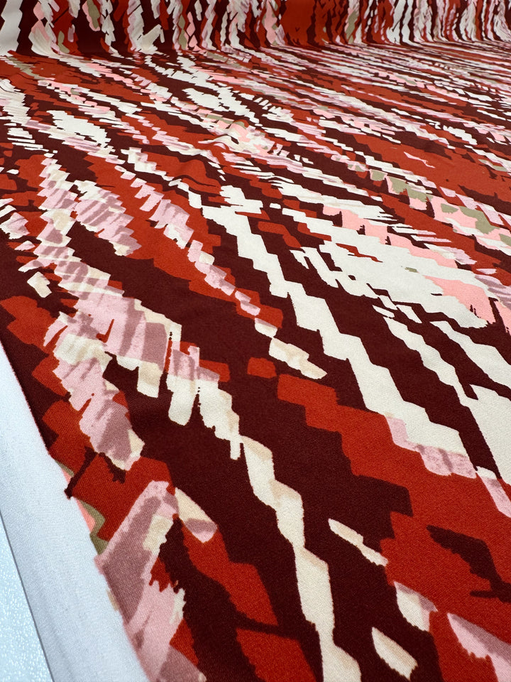 A close-up view of Super Cheap Fabrics' Printed Lycra - Crimson Crush - 150cm shows abstract, jagged patterns in red, pink, and white for a dynamic zigzag effect, reminiscent of popular medium weight lycra designs.
