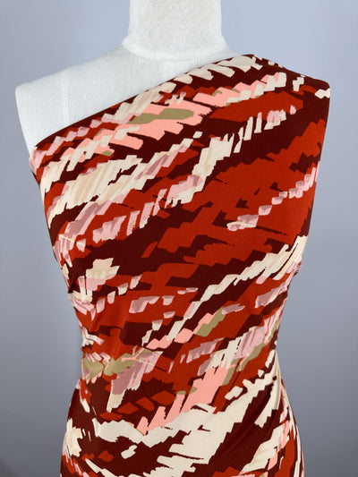A mannequin displays Super Cheap Fabrics’ Printed Lycra - Crimson Crush (150cm), featuring bold, abstract red, pink, cream, and beige brushstrokes on medium-weight fabric with a beautiful drape.