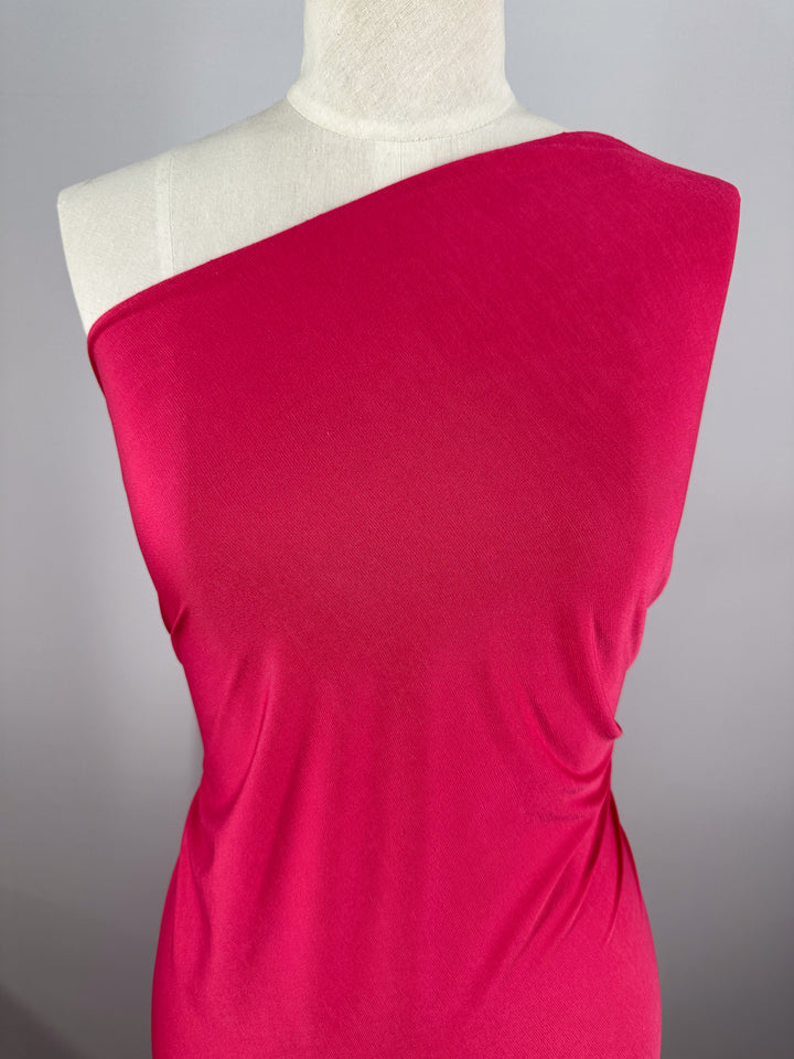 A mannequin displays the ITY Knit - Bright Rose - 150cm from Super Cheap Fabrics, a smooth, medium-weight fabric that drapes effortlessly and forms subtle folds, set against a neutral gray background.