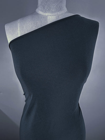 A mannequin wears a fitted, one-shoulder dress made from Super Cheap Fabrics' ITY Knit - Dark Slate (150cm), a medium-weight polyester spandex, standing against a plain gray background. One shoulder is covered, the other left bare.