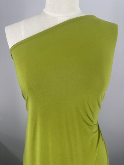 A dress form showcases a lime green, one-shoulder, sleeveless garment made from Super Cheap Fabrics' ITY Knit - Golden Cypress (150cm), featuring soft gathered details on one side, set against a plain gray background.