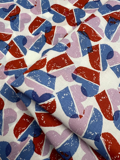Super Cheap Fabrics’ Printed Cotton - Berry Candy Hearts - 148cm features a vibrant red, blue, and purple heart pattern with a textured look on white 100% cotton, offering comfort and durability.
