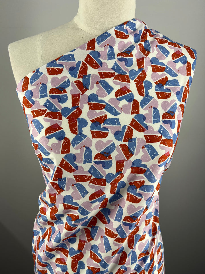Super Cheap Fabrics' Printed Cotton - Berry Candy Hearts - 148cm is a 100% cotton fabric featuring colorful abstract red, blue, and purple heart shapes overlapping on a white background, displayed draped over a mannequin.