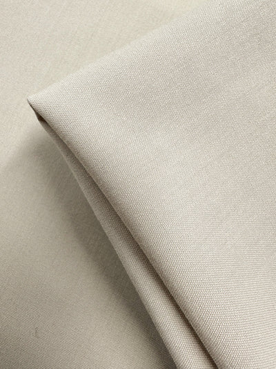A close-up of Suiting - Oatmeal - 150cm by Super Cheap Fabrics shows folded, medium-weight beige fabric with a smooth, slightly textured surface and fine even weaving.