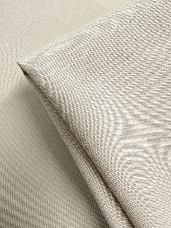 A close-up of Suiting - Oatmeal - 150cm by Super Cheap Fabrics shows folded, medium-weight beige fabric with a smooth, slightly textured surface and fine even weaving.