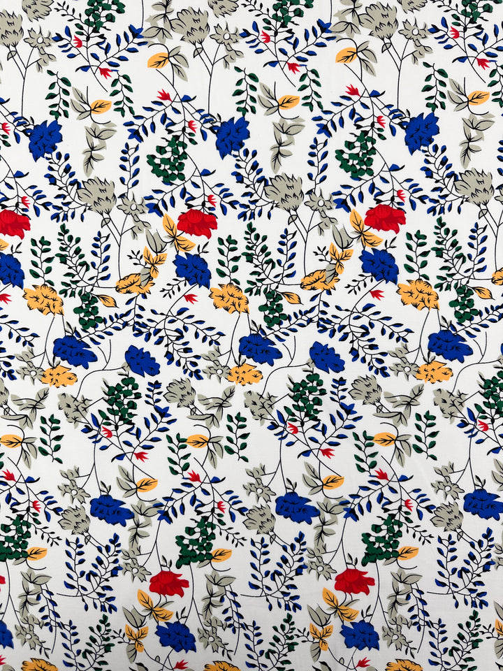Designer Rayon - Petal Grid by Super Cheap Fabrics features a colorful floral pattern with red, yellow, blue, and gray flowers plus green leaves on white rayon fabric in a repeating, symmetrical design. Width: 145cm.