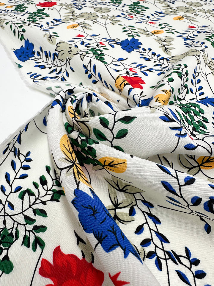 Designer Rayon - Petal Grid by Super Cheap Fabrics is a white, lightweight rayon fabric (145cm wide) featuring a smooth texture and vibrant floral print in blue, red, yellow, and green leafy branches.