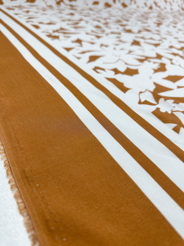 A close-up of Designer Rayon - Clay Fade (145cm) from Super Cheap Fabrics, displaying a brown and white floral pattern with bold brown stripes and detailed white flower motifs on a smooth, versatile surface.