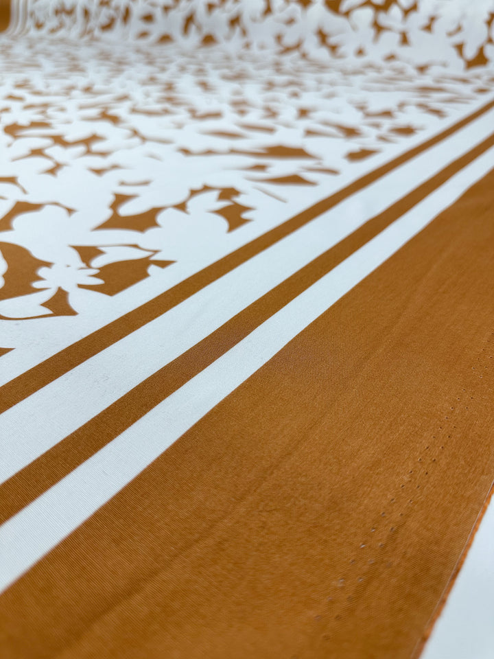 Close-up of Designer Rayon - Clay Fade by Super Cheap Fabrics: a white and brown fabric with diagonal floral motifs and stripes. At 145cm wide, its vibrant pattern and soft texture make it perfect for chic, versatile creations.