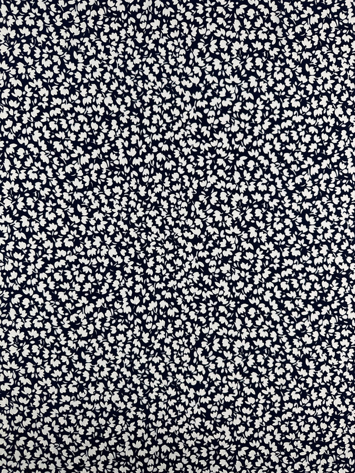 A close-up of Super Cheap Fabrics' Textured Lycra - Night Bloom Micro (150cm) shows a medium weight fabric with a dense scattering of small white floral patterns on a dark background, creating an intricate and lively design.