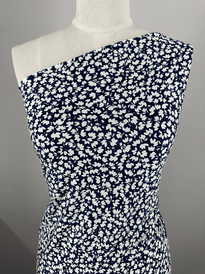 A mannequin showcases Super Cheap Fabrics' Textured Lycra - Night Bloom Micro (150cm), featuring a white floral print on navy in a one-shoulder style, set against a neutral background.