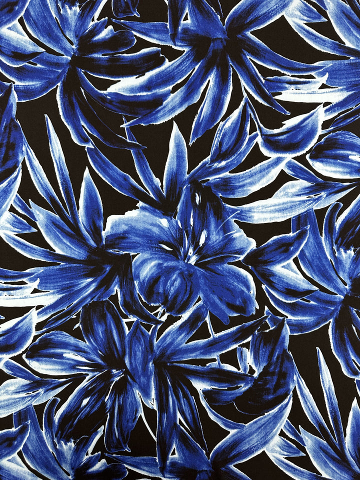 Super Cheap Fabrics' Printed Lycra - Cobalt Charge - 150cm features bold blue and white tropical flowers with painterly brushstrokes on a black background, creating a vibrant, energetic look on medium weight lycra.