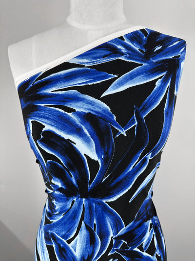 A close-up of a dress form displays a one-shoulder garment made from Super Cheap Fabrics' Printed Lycra - Cobalt Charge (150cm), featuring bold blue and black floral patterns on a white background.