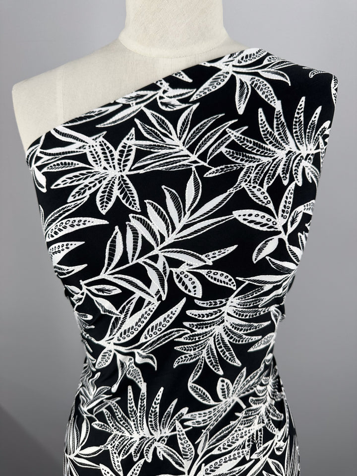 A mannequin showcases a black, one-shoulder outfit made from Super Cheap Fabrics' Textured Lycra - Shadow Fern (150cm), featuring a striking white tropical leaf design.