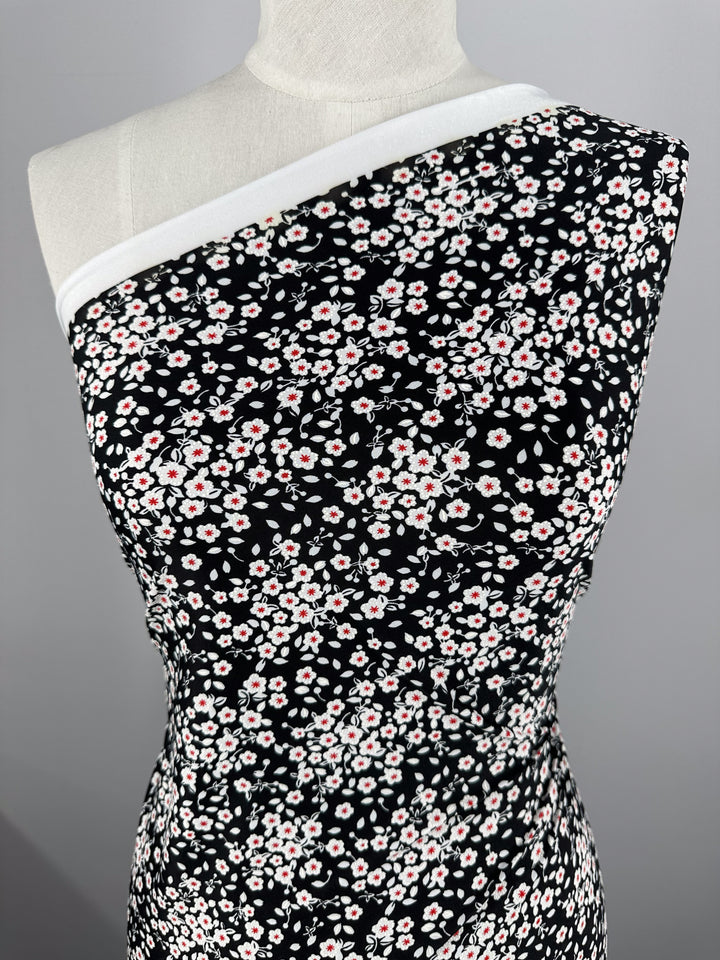 A mannequin showcases Super Cheap Fabrics' Textured Lycra - Sugar Pollen (150cm), featuring a black base with a white and red small floral pattern, styled in a one-shoulder look that reveals the neckline and left shoulder.