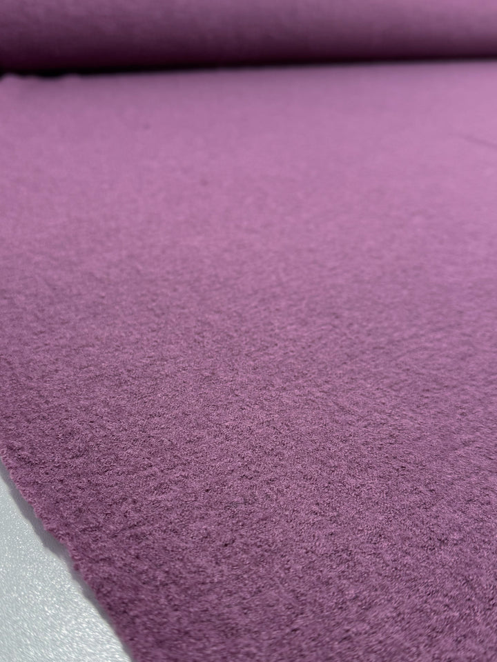 A close-up of Super Cheap Fabrics’ Boiled Wool – Mauve Orchid (142cm) shows the soft, slightly fuzzy texture of this purple fabric unrolled on a flat surface.