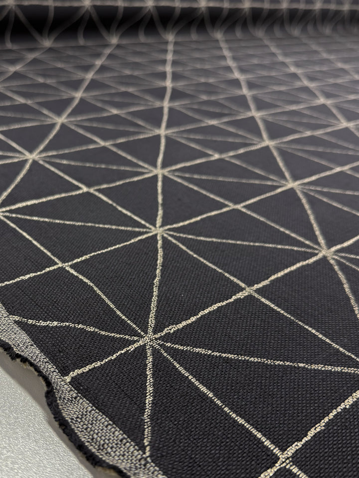 Close-up of Super Cheap Fabrics' Linen Viscose - Quentin Coal (156cm), showing heavy-weight upholstery fabric with a geometric pattern of intersecting light lines forming triangles and diamonds across the surface; fabric edge visible in foreground.