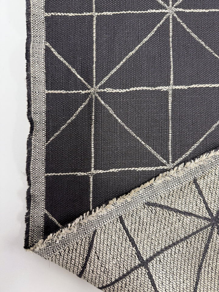 A close-up of Super Cheap Fabrics' Linen Viscose - Quentin Coal (156cm), featuring a black fabric with a white geometric grid pattern. Both front and reversed, lighter back are shown with slightly frayed edges. Perfect for upholstery projects.