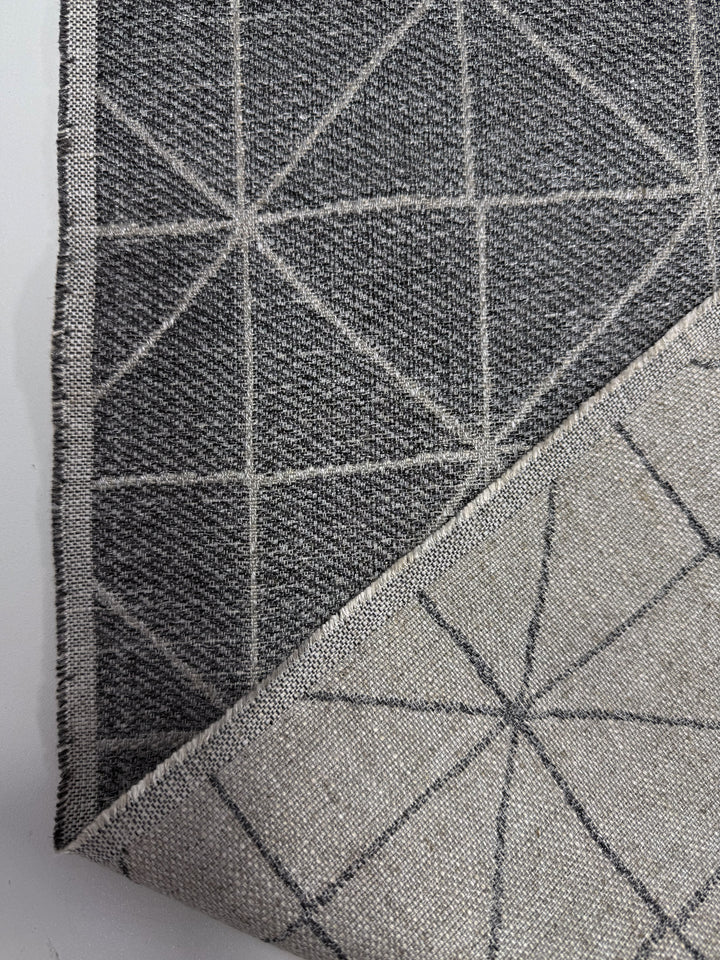 Close-up of Linen Viscose - Quentin Silver (156cm) by Super Cheap Fabrics: gray fabric with a white-lined geometric triangle pattern. One corner is folded to show the lighter, inverted reverse. Limited stock available.