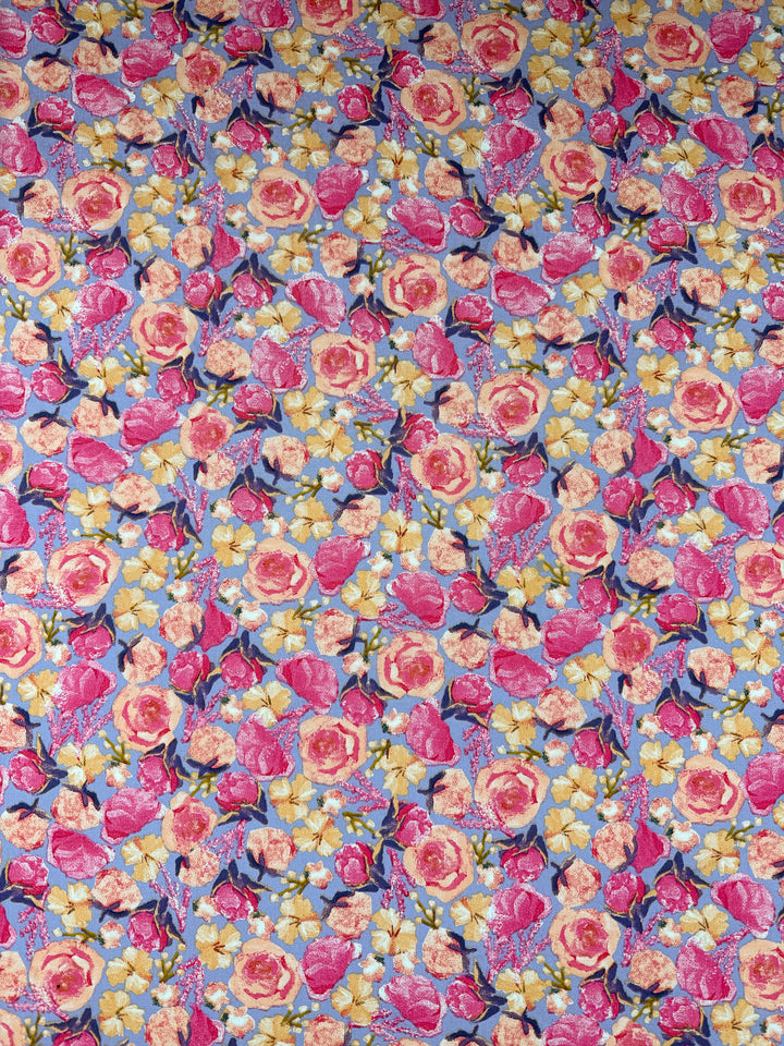 Super Cheap Fabrics' Designer Rayon - Botanic Crush (142cm) showcases a vivid floral print with pink and yellow blooms and green leaves on a light blue base, making it a versatile fabric for creating lively, colorful projects.